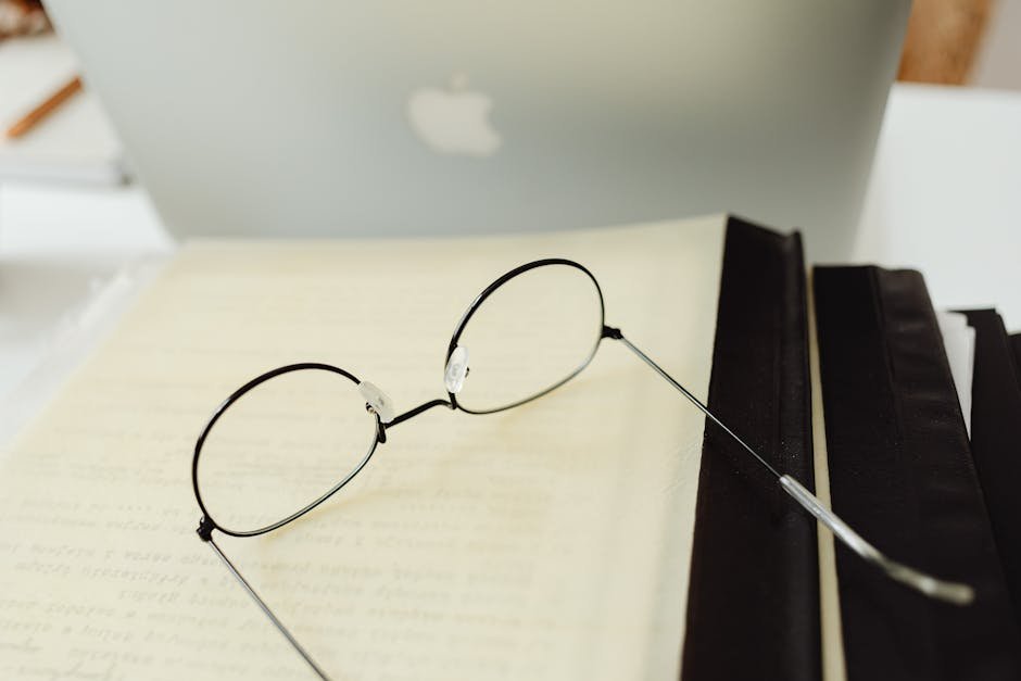 Round eyeglasses resting on an open book beside a laptop in a quiet study atmosphere.